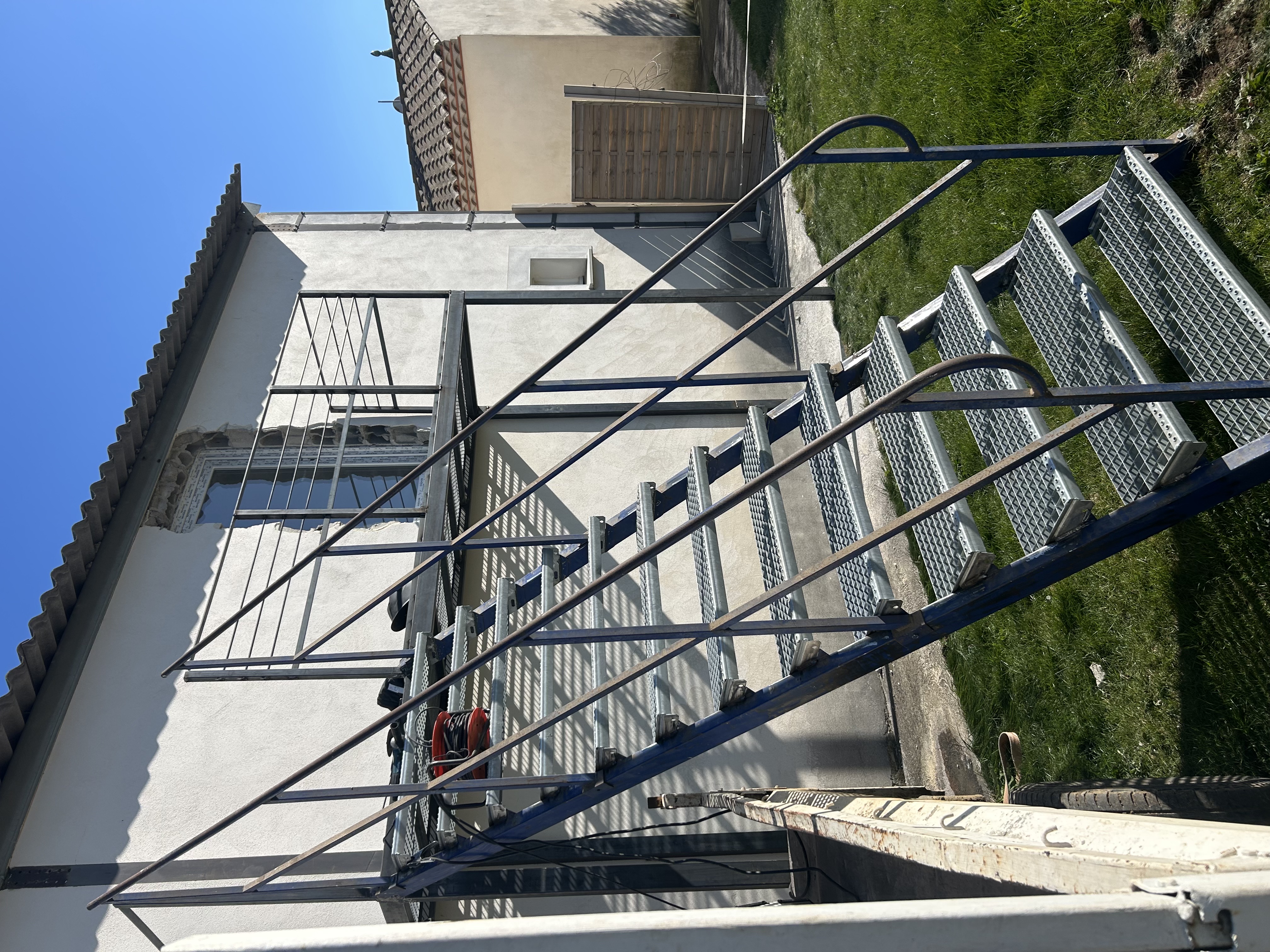 Escalier métallique extérieur droit avec marches en caillebotis antidérapant et garde-corps sécurisé.